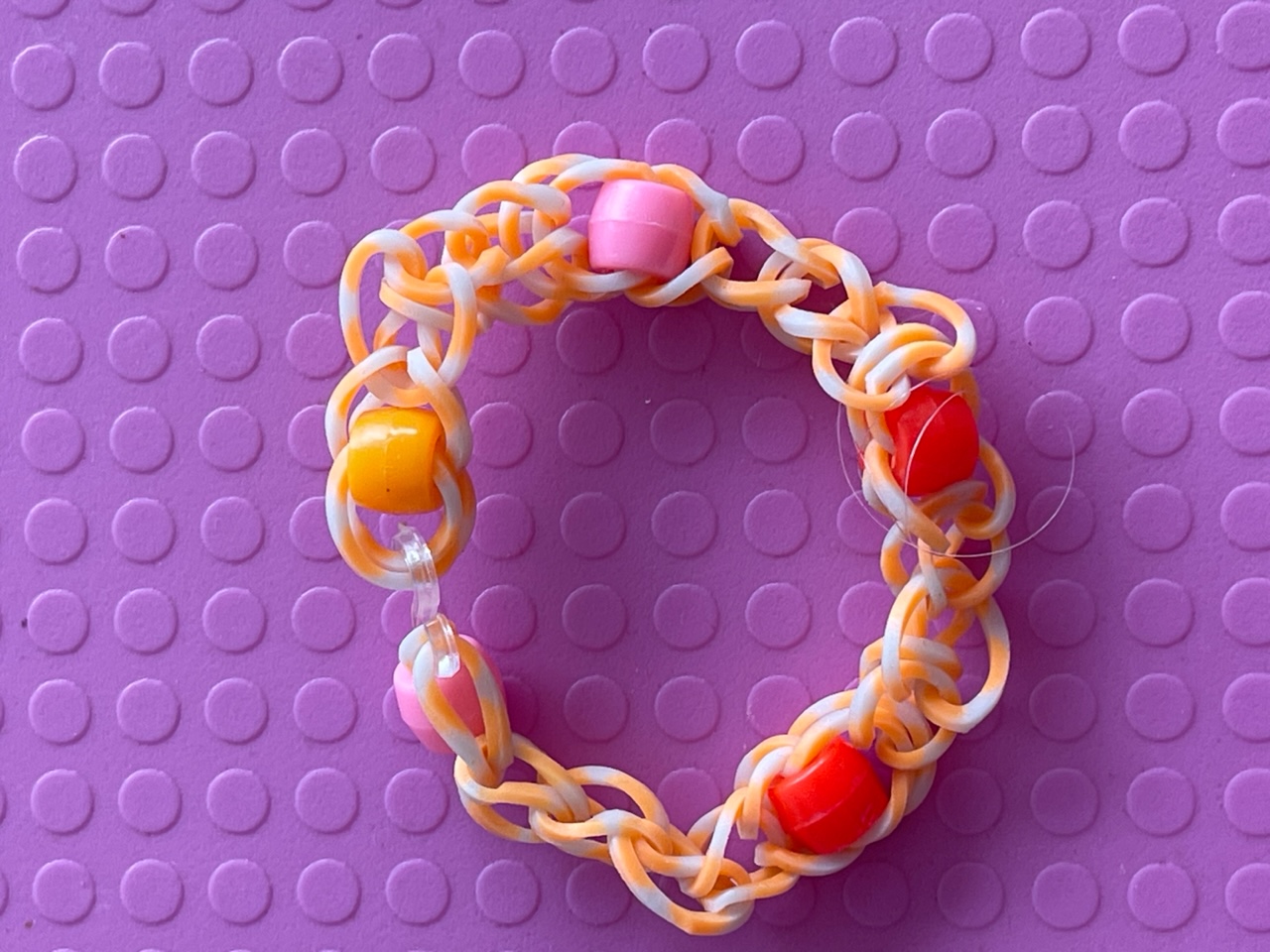 Armband av sammaflätade små färgglada gummisnoddar och pärlor.