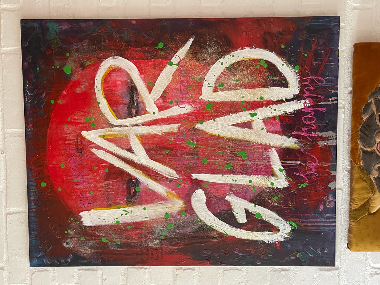 Målad tavla med texten "Var glad" i förgrunden och ett ansikte i bakgrunden