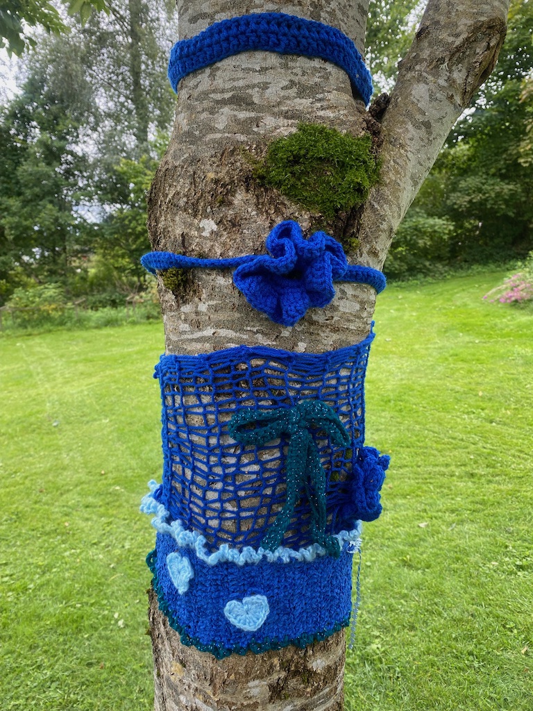 Blåa stickade och virkade band runt ett träd.