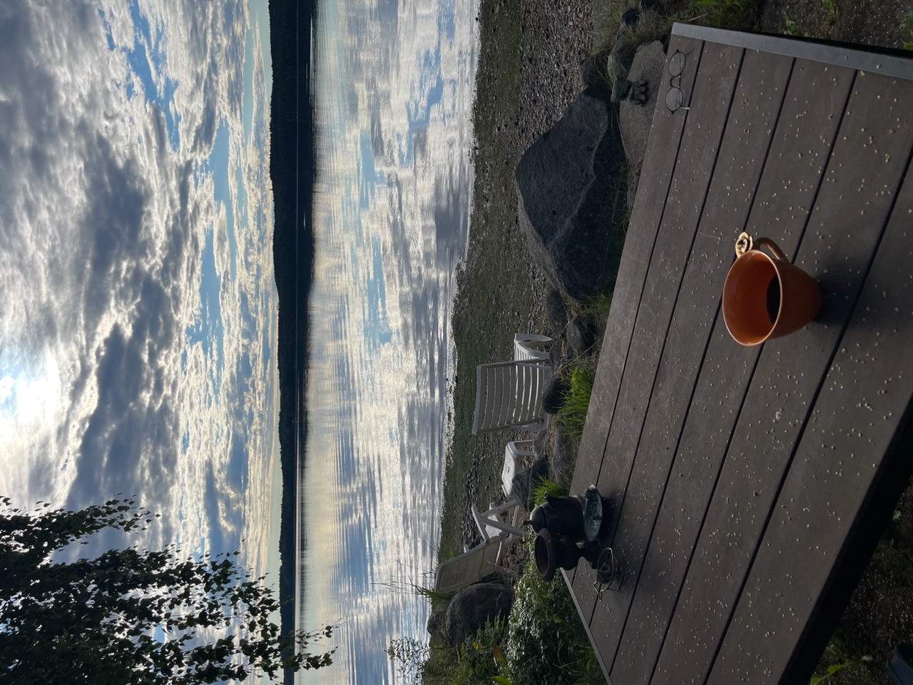 En kaffekopp på utemöbel, solstol på stand och vy över sjön