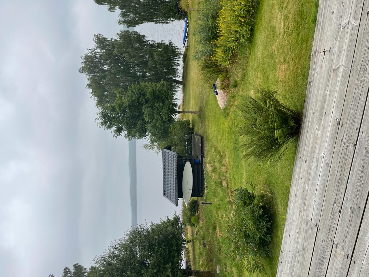 Vy grössluttning med gästhus, träd och sjö i bakgrunden