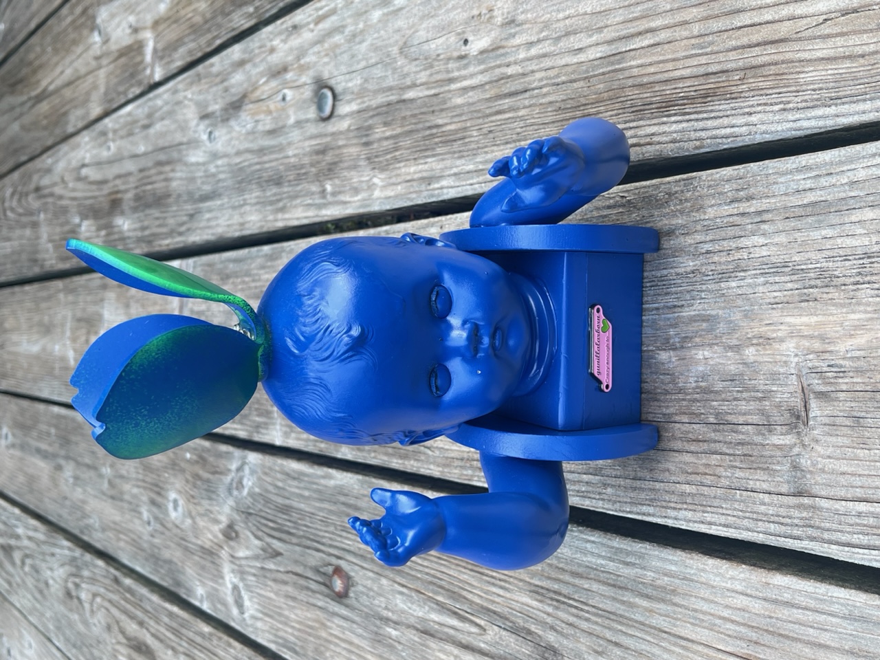 Blå skulptur med dockhuvud och dockarmar på en liten dockstol